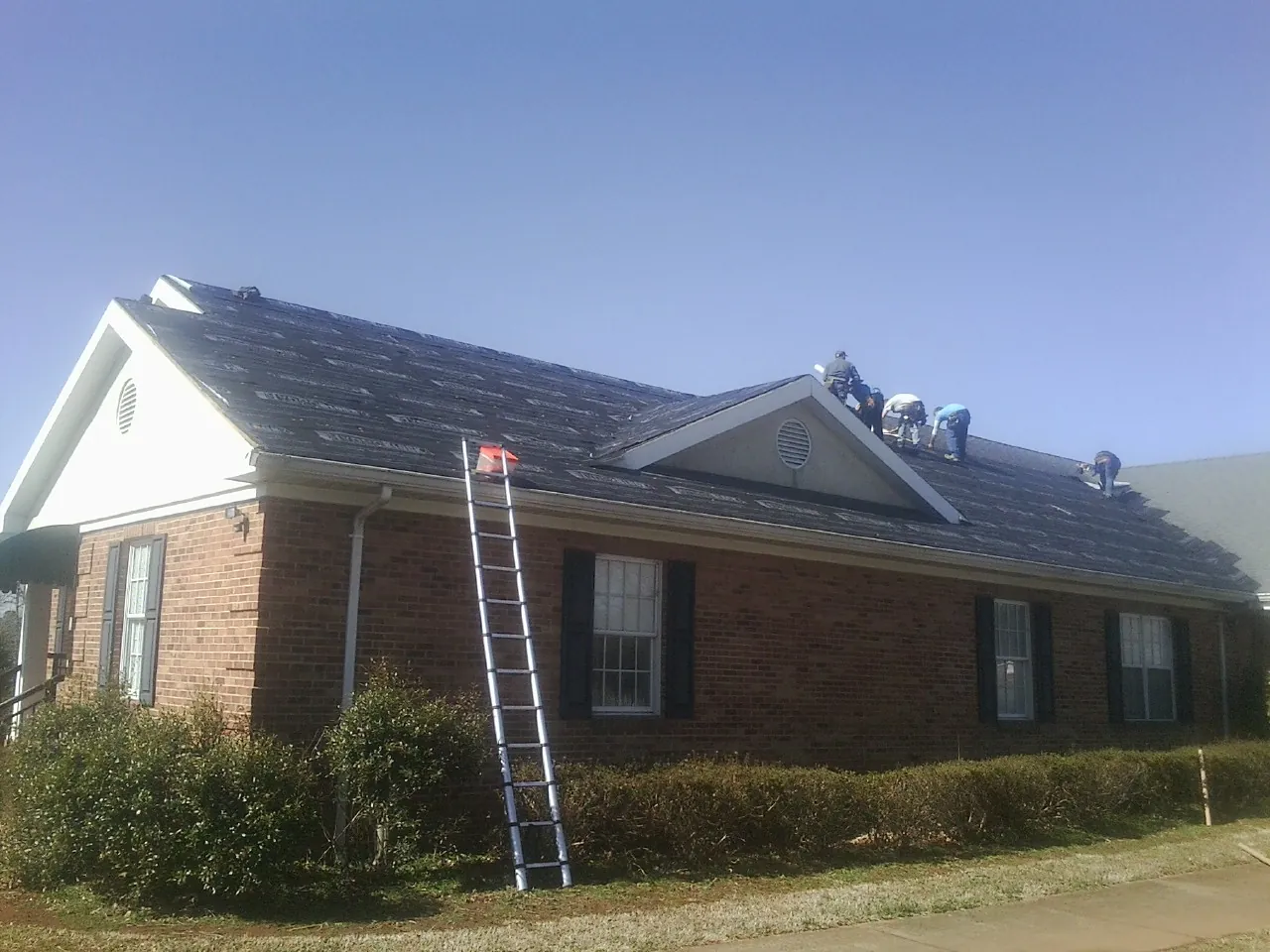 Crew tearing shingles off a brick ranch roof with a ladder set — Emergency Roof Repair work by our crew in Fredonia