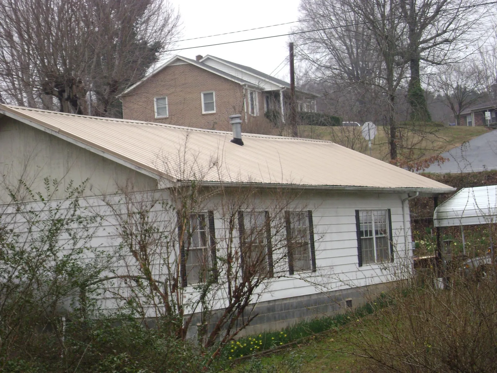 Tan metal roof on a white sided house set into a hillside — Commercial Roofing by Roofing Brothers in Fredonia